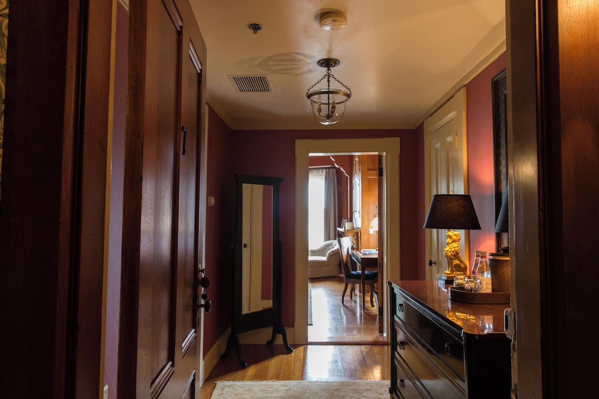 A hallway with wooden doors, a mirror, a chandelier, and a dining area in the background.
