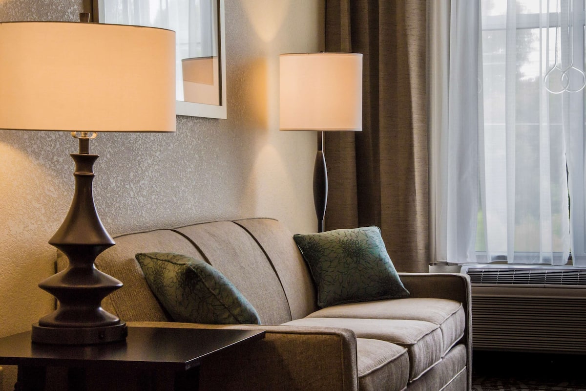Ein Hotelzimmer mit einer Couch, zwei Lampen, einem Spiegel und einem Fenster mit Vorhängen.