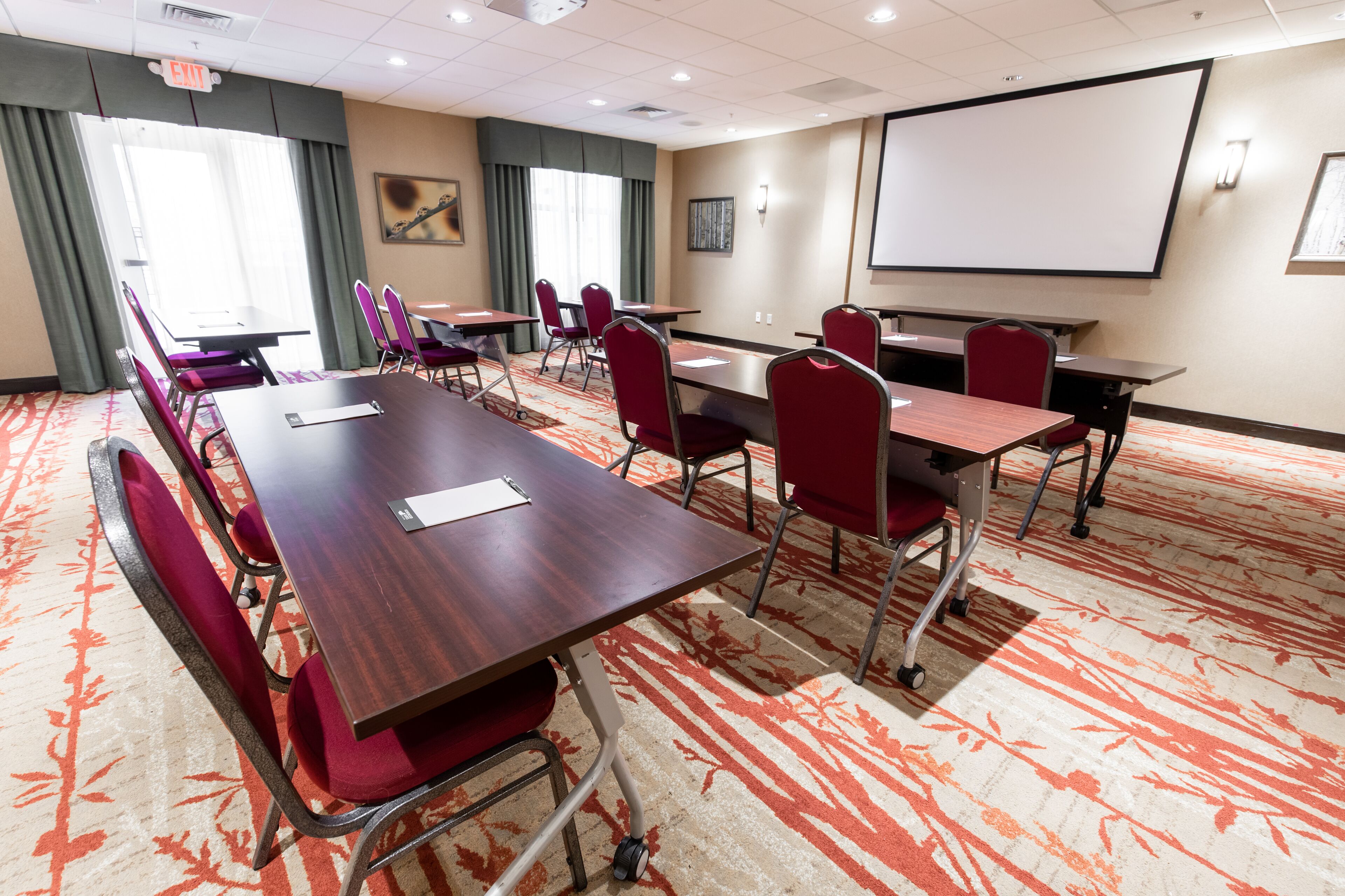 A conference room with a large table, multiple chairs, a projector screen, and a carpeted floor.