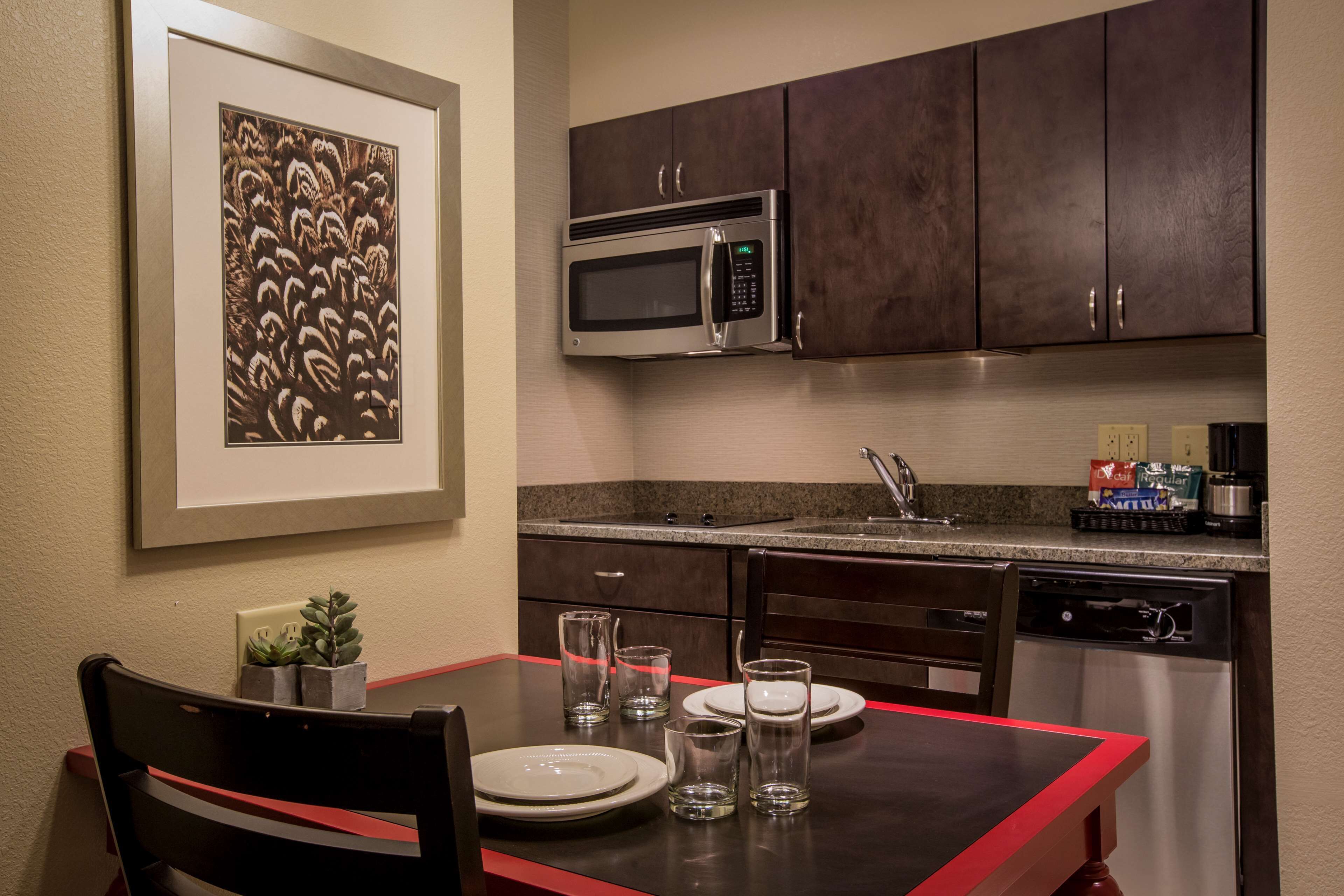 A kitchen with a microwave, dishwasher, and a dining table set with plates and glasses.