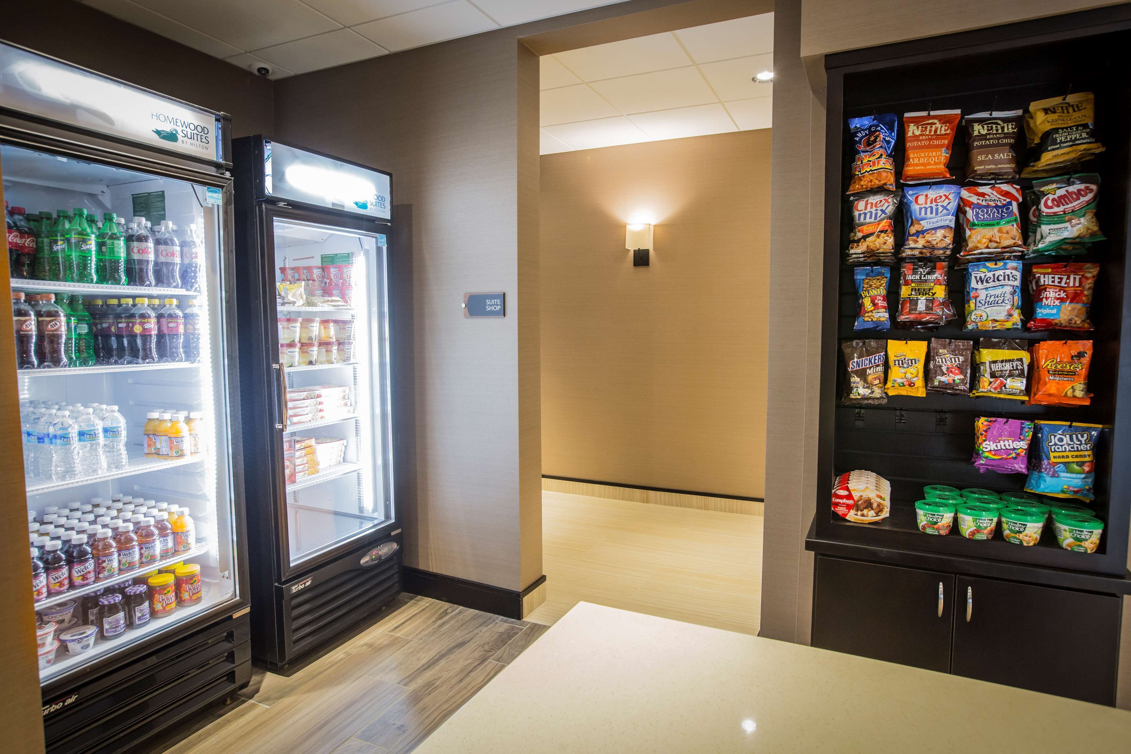 A hotel room with a minibar, a refrigerator stocked with beverages, and a snack shelf.