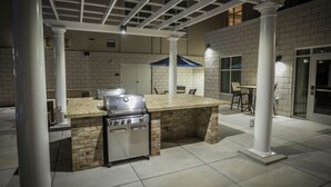 An outdoor kitchen area with a grill, a bar counter, and a seating area with chairs and a table. - Homewood Suites by Hilton Charlotte Ballantyne, NC (Charlotte)
