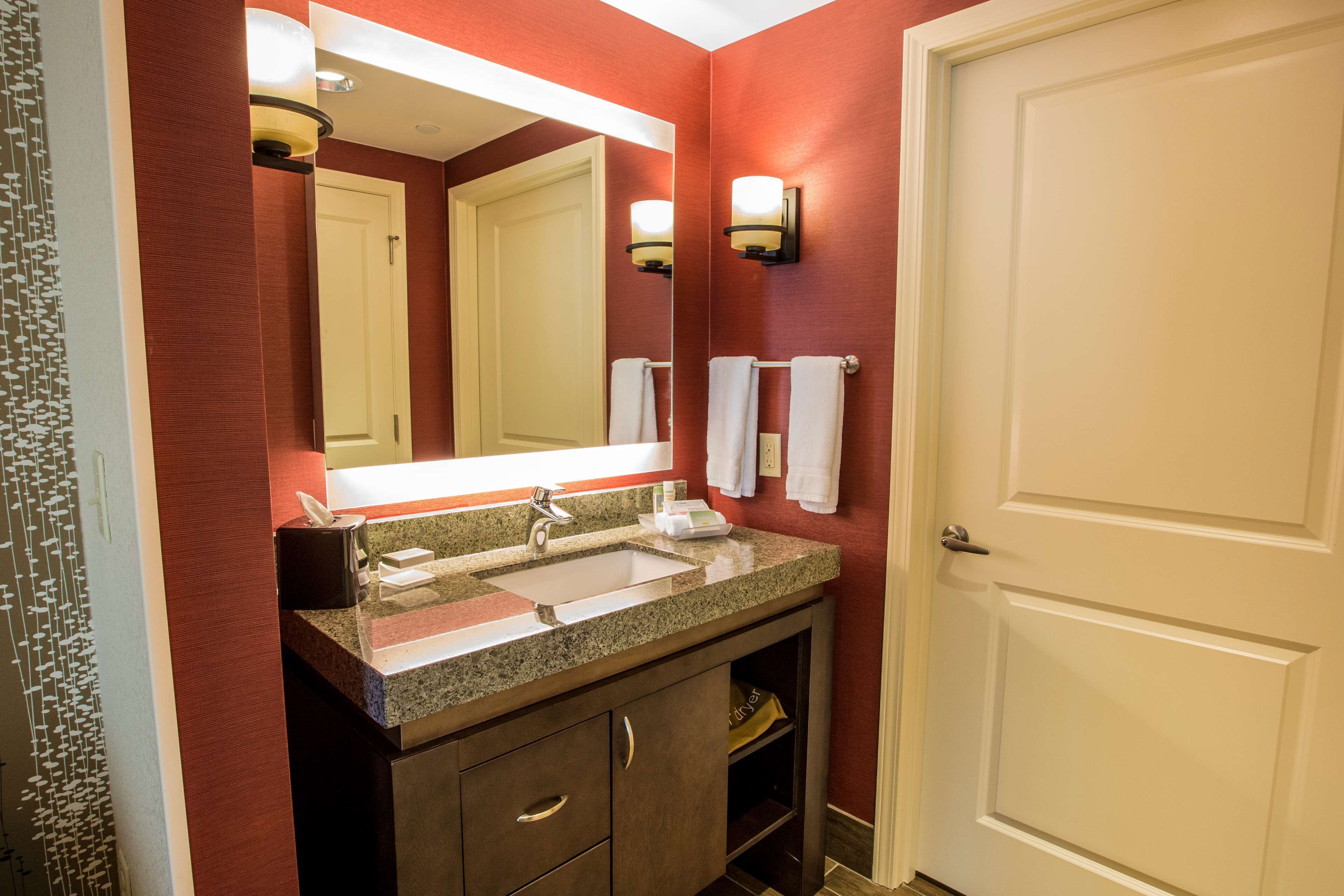 A bathroom with a granite countertop sink, a mirror, a towel rack, and a door.