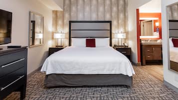 Ein Hotelzimmer mit einem großen Bett, einem Fernseher, einem Schreibtisch mit Schubladen, einem Spiegel und einem Badezimmer mit Waschbecken und Spiegel.