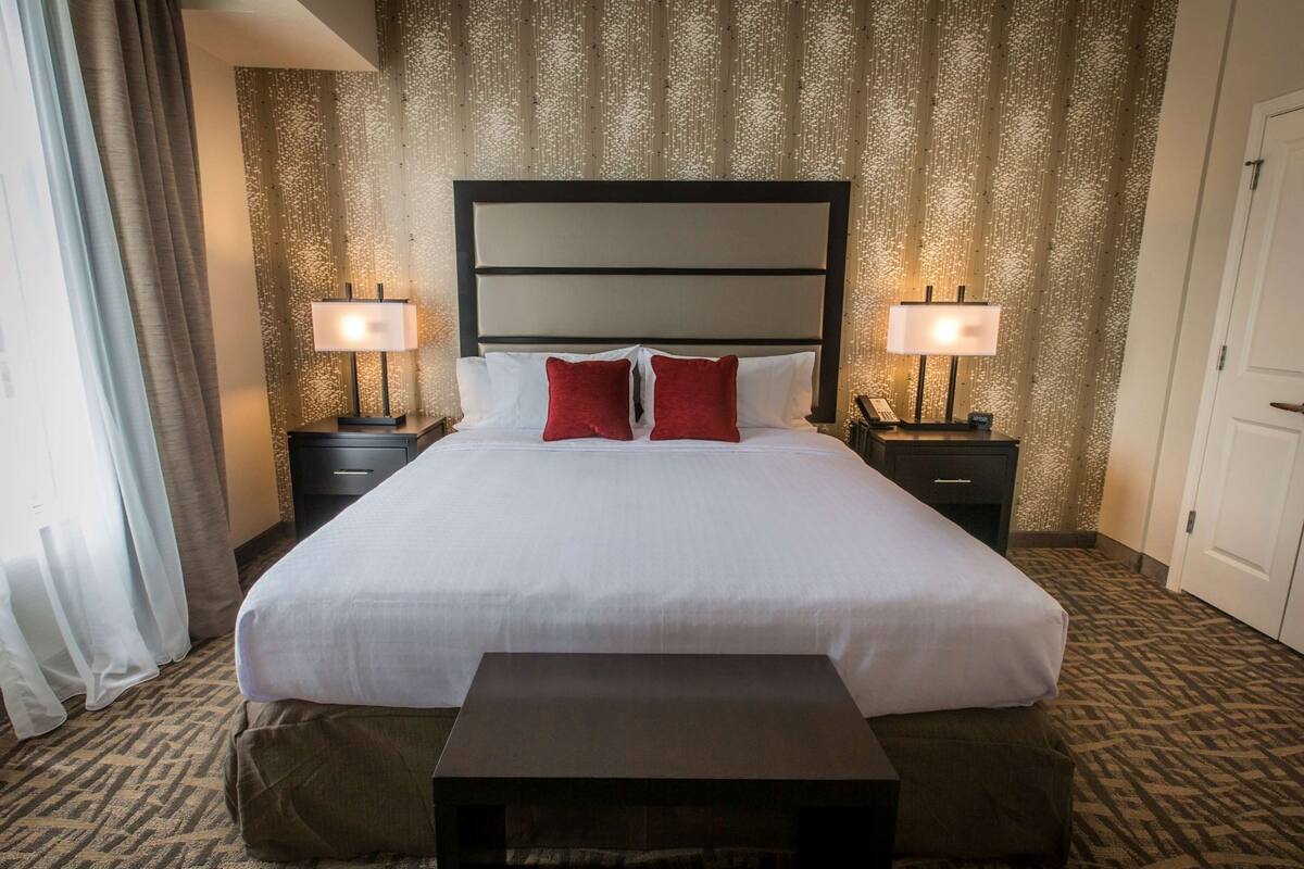 Ein Hotelzimmer mit einem großen Bett, zwei Nachttischen mit Lampen, einem Beistelltisch und einem Teppich mit Muster.