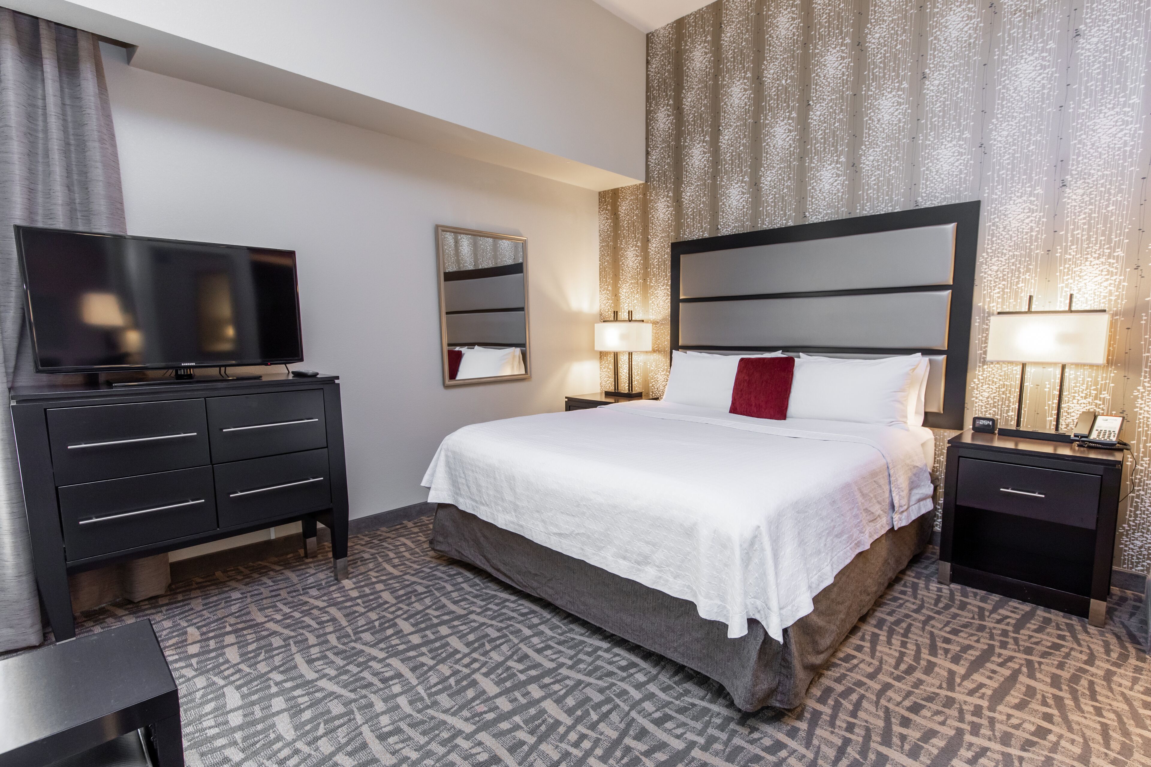 A hotel room with a bed, bedside lamps, a TV, a dresser, and a nightstand.