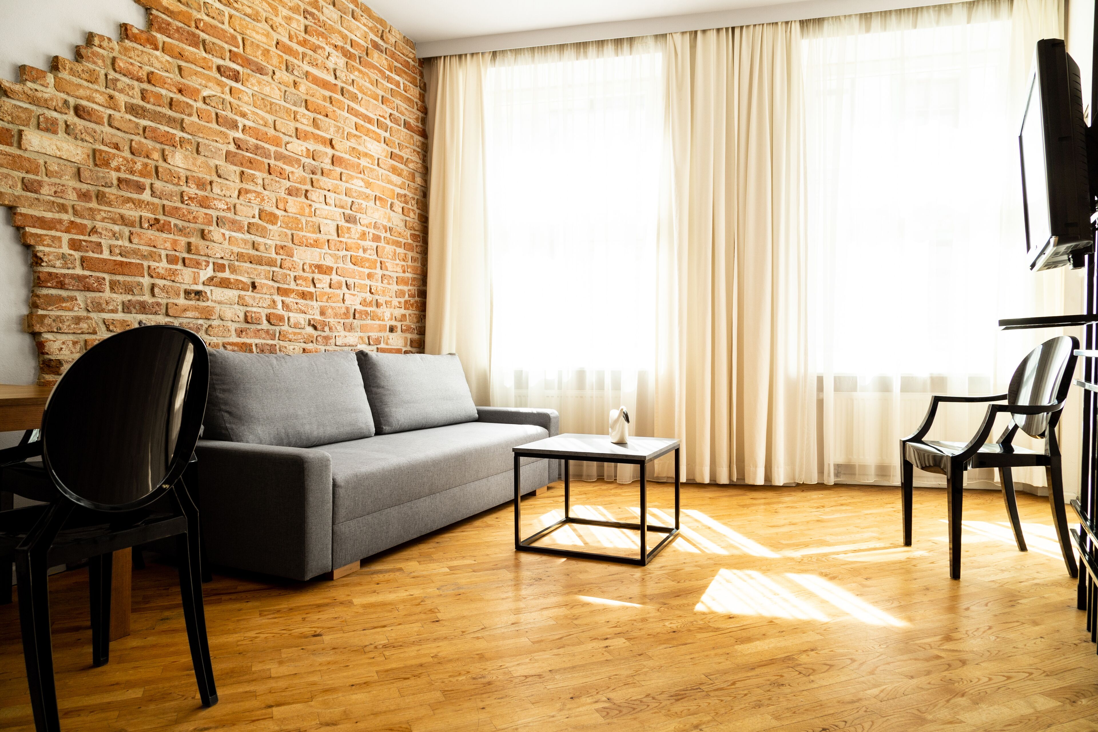 Ein modernes Wohnzimmer mit Backsteinwand, grauem Sofa, Holzboden und an der Wand montiertem Fernseher.