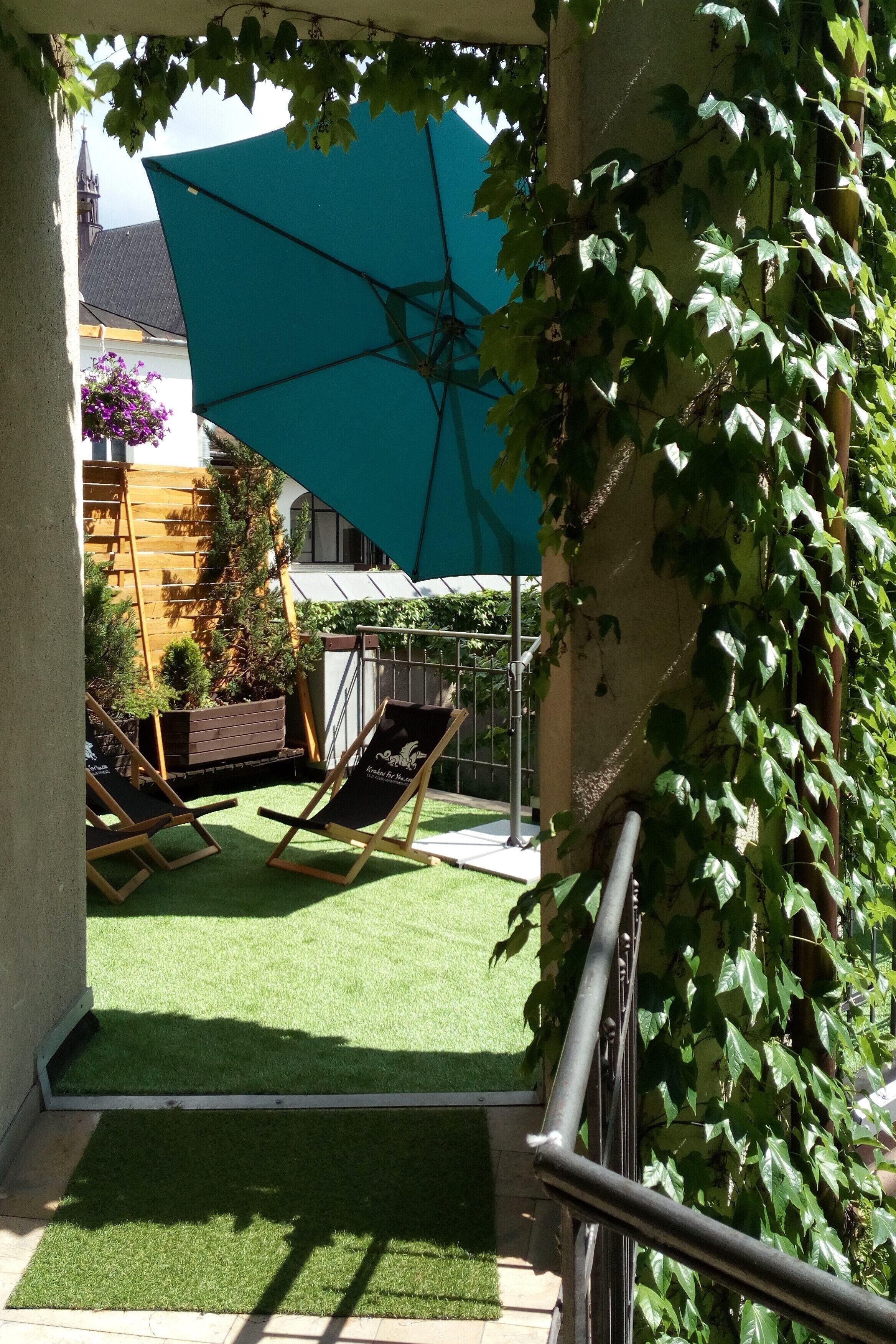 Un patio con césped artificial, una sombrilla azul y una silla de madera.