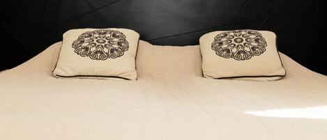 Una cama con cubrecolcha beige acolchado y dos almohadas con diseños negros elaborados.