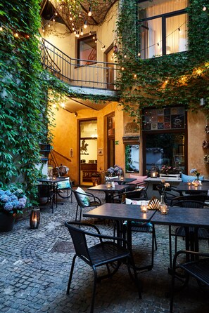 An outdoor café with tables and chairs, a cobblestone floor, and a staircase leading to an upper level. - Krakow For You (Kraków)