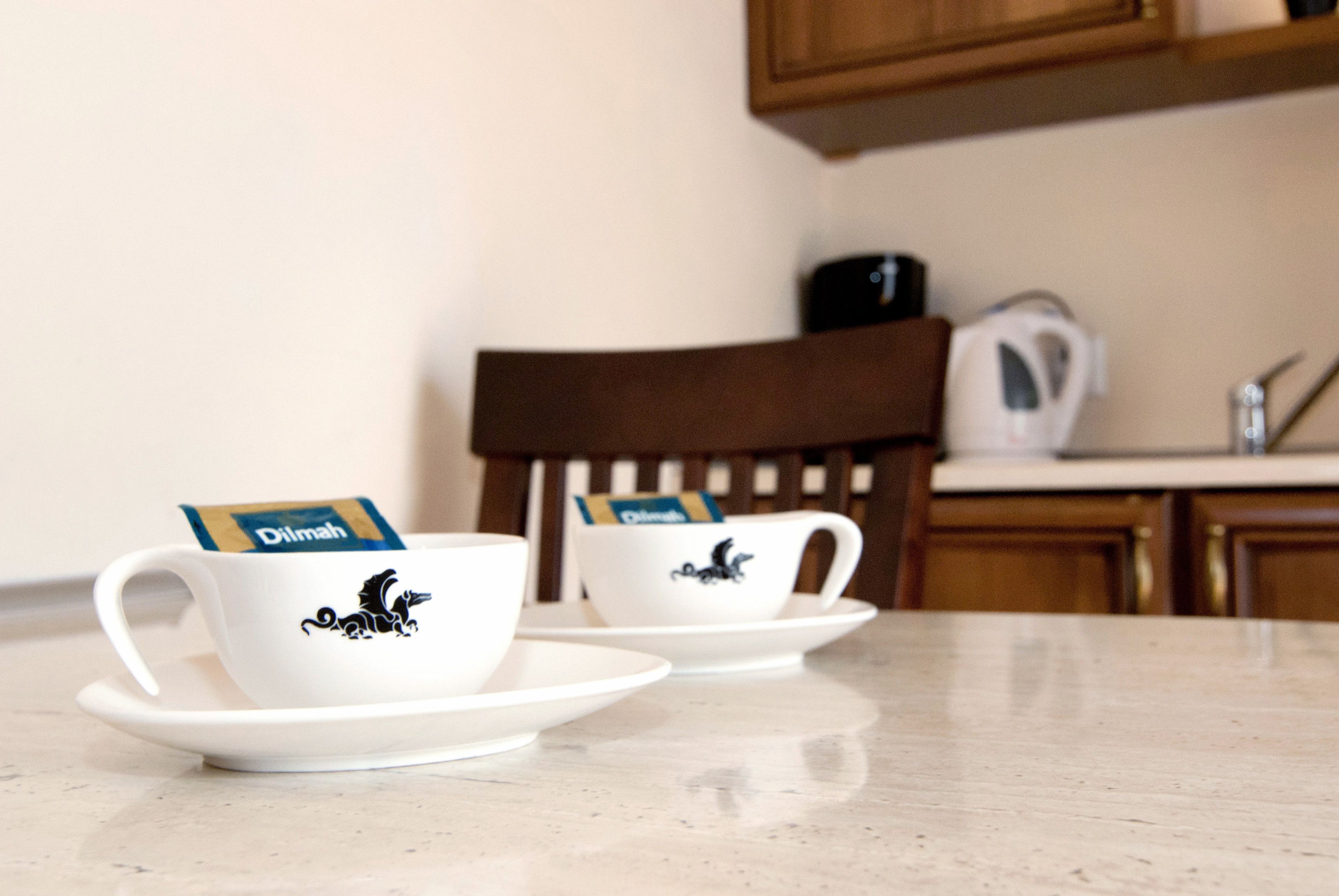Dos tazas blancas con un diseño de dragón negro, cada una con una bolsita de té Dilmah, sobre un platito blanco.