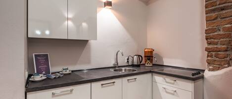 A modern kitchen with white cabinets, a black countertop, a stainless steel sink, and a coffee machine.