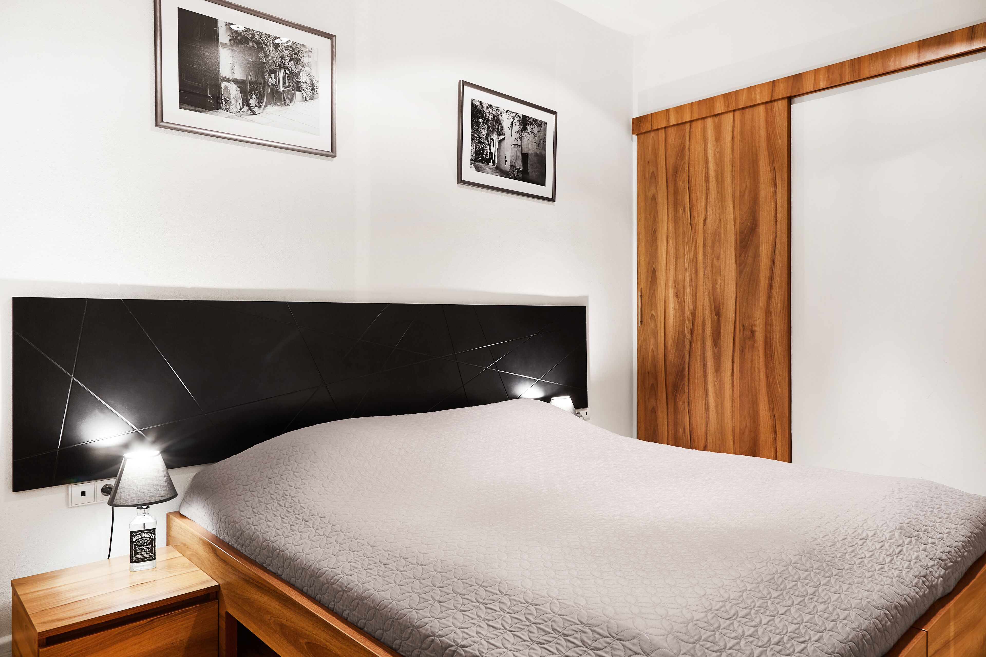 A bedroom with a bed, bedside table, lamp, and two framed pictures on the wall.