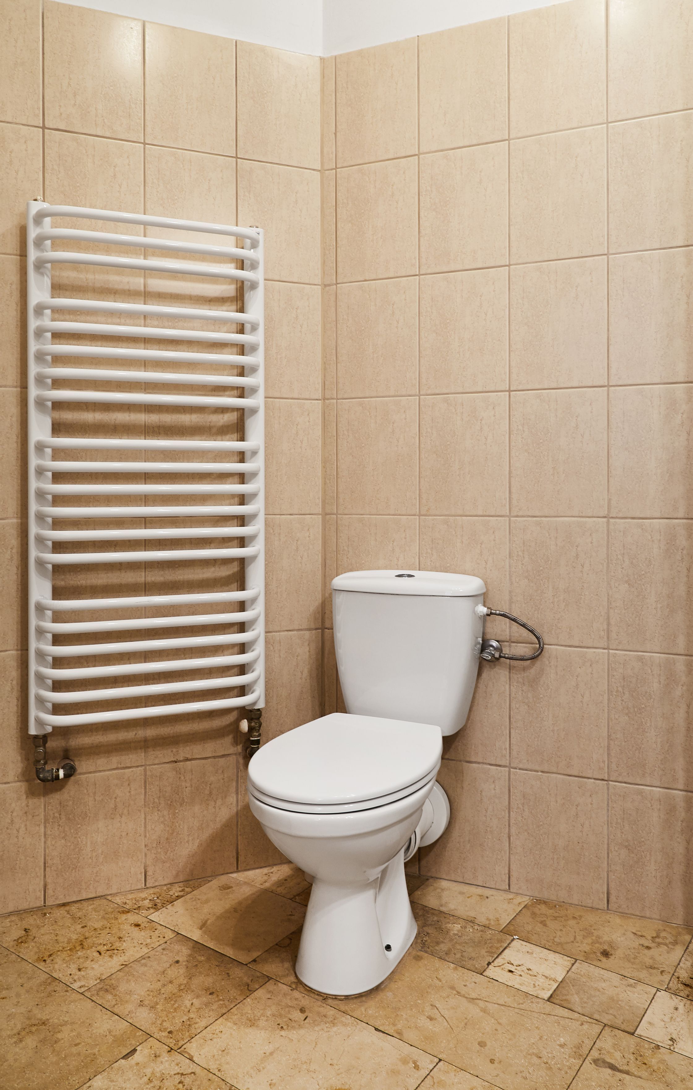 Une salle de bain avec des toilettes, un radiateur blanc et des murs et un sol carrelés de couleur beige.