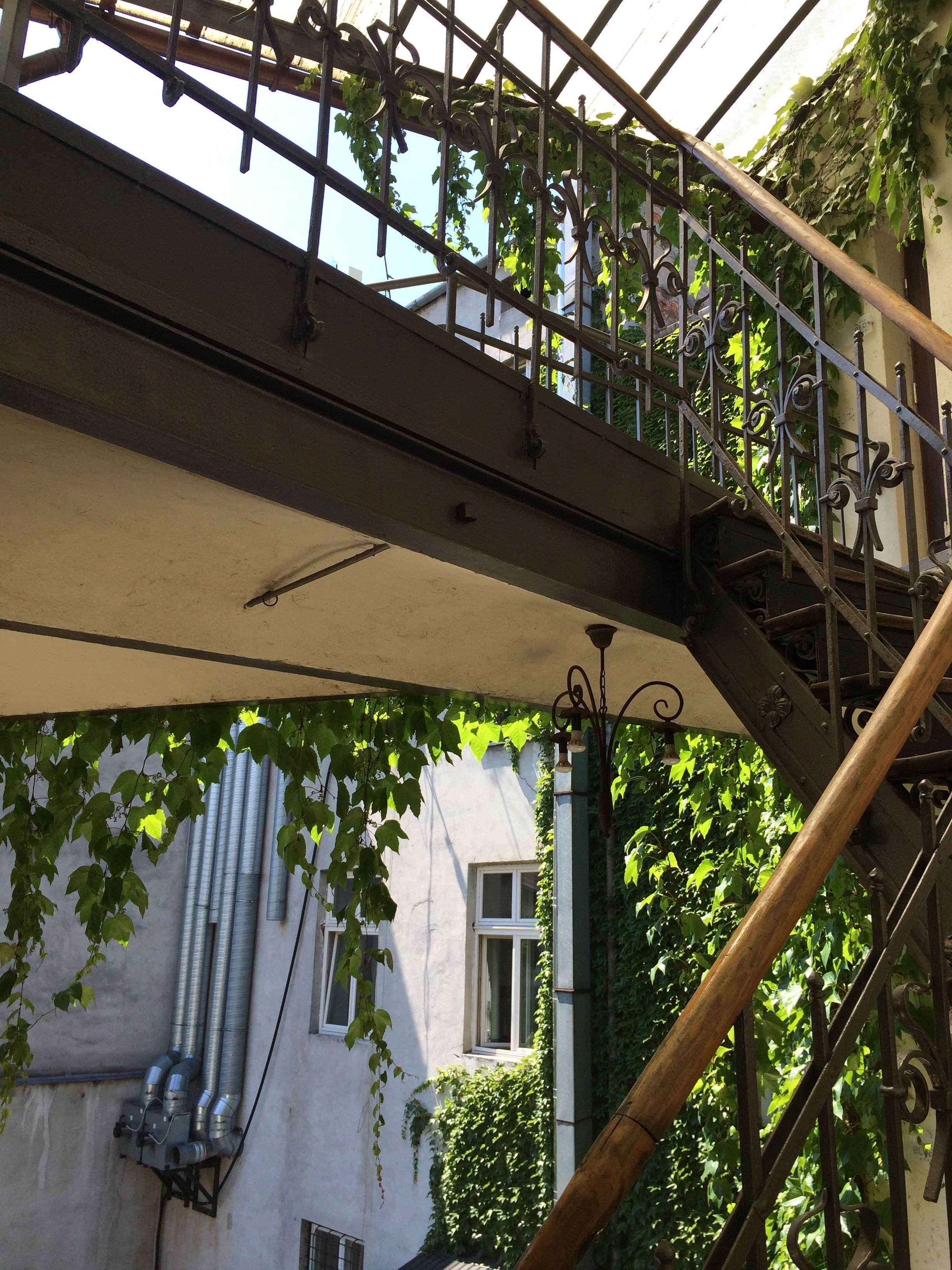 A metal staircase with ornate railings and a view of a building with ivy-covered walls and windows.