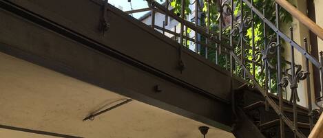 Una escalera de metal con barandillas ornamentales y vistas a un edificio con paredes cubiertas de hiedra y ventanas.