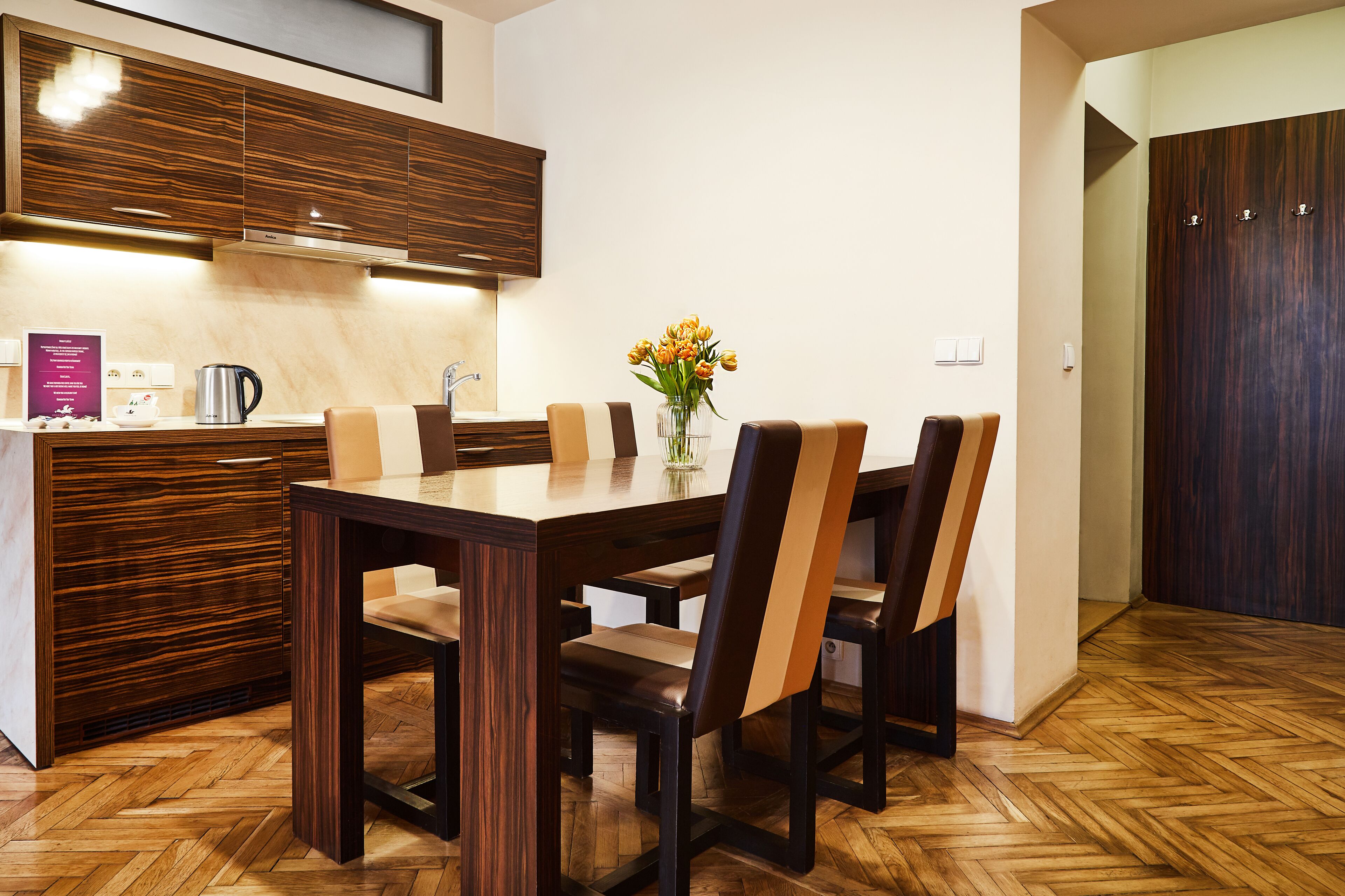 A modern kitchen with wooden cabinets, a dining table with chairs, and a vase with flowers on the table.