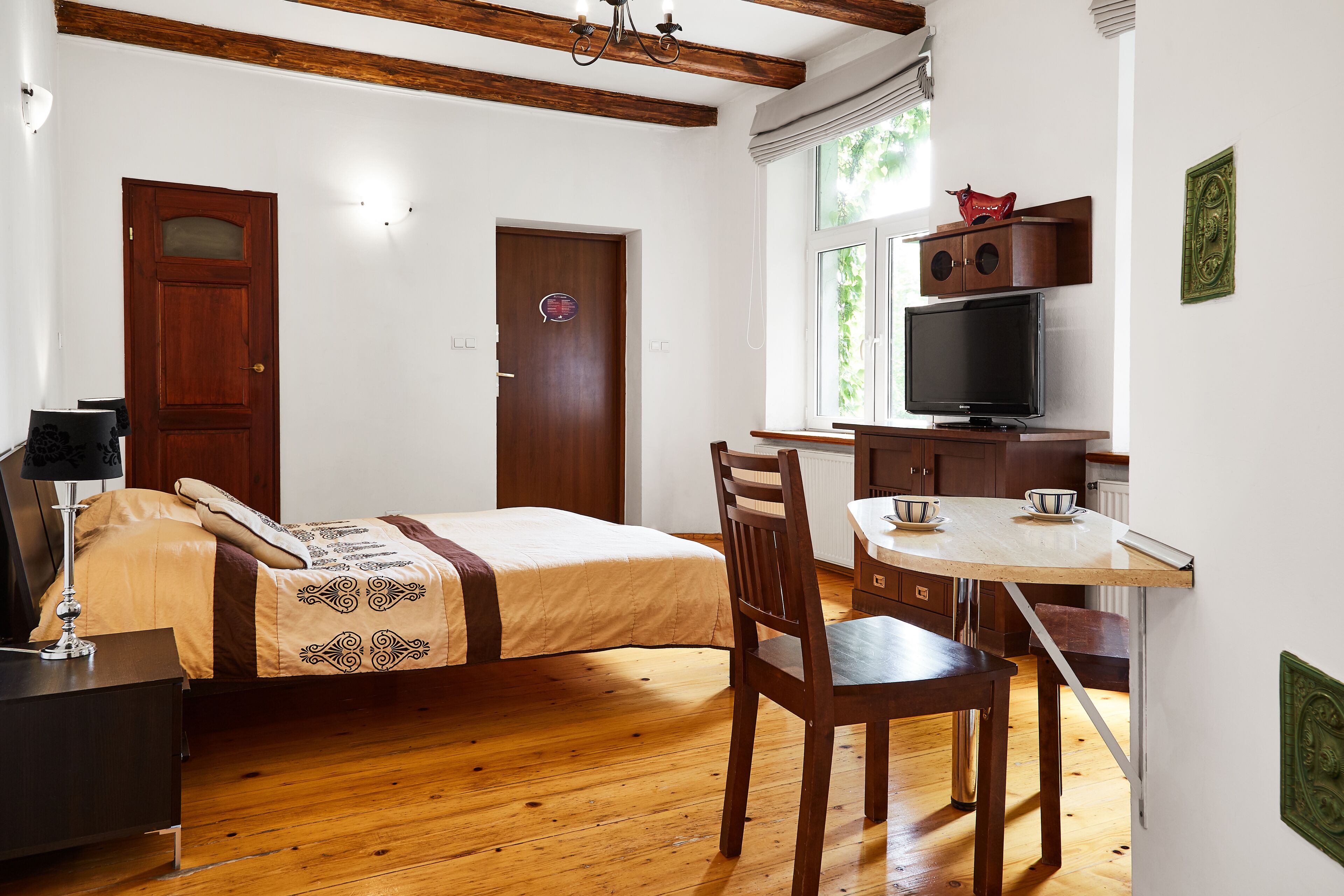 A bedroom with a bed, a desk with a chair, a television, and a window with blinds.