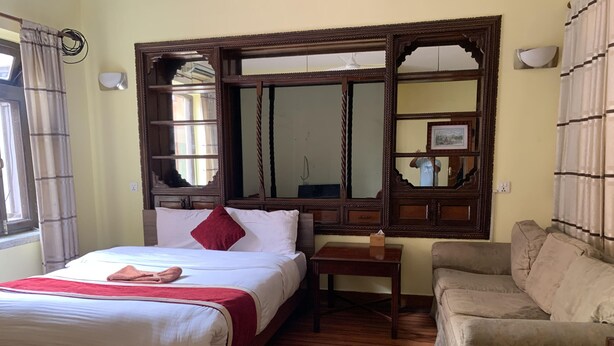 Habitación de hotel con cama, mesita de noche de madera, sofá y un espejo grande con marco decorativo.