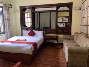 A hotel room with a bed, a wooden nightstand, a sofa, and a large mirror with a decorative frame. - Hotel Buddha Home Nepal (Kathmandu)