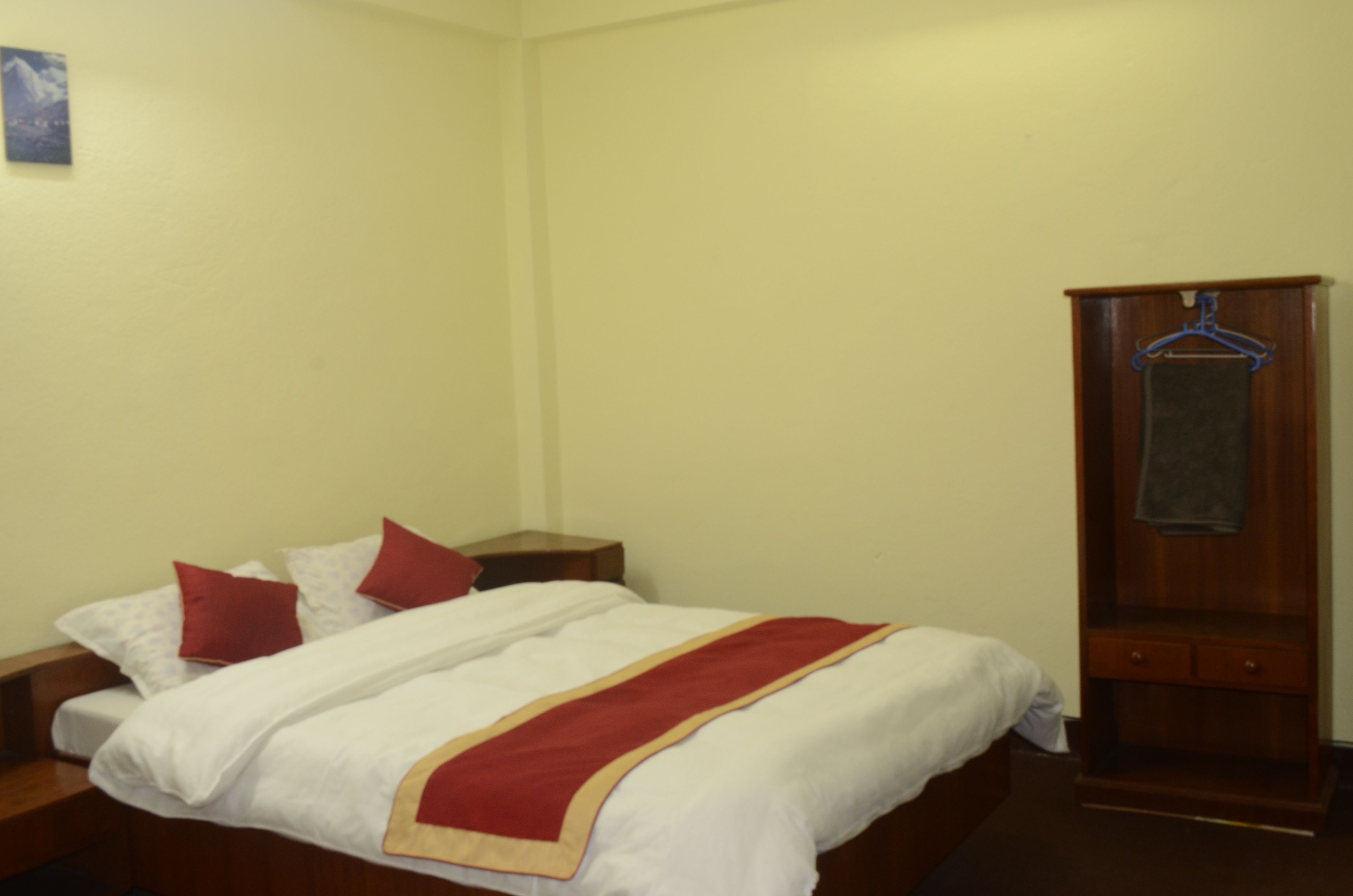 A hotel room with a neatly made bed, a wooden wardrobe, and a small bedside table.