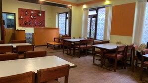 Un restaurante con mesas y sillas de madera, una zona de bar con botellas y ventanas con cortinas.