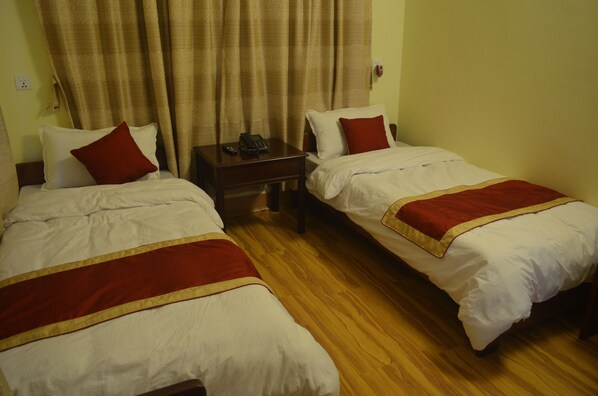 Two single beds with red and white bedding, a wooden nightstand with a phone, and a curtain with a patterned design.