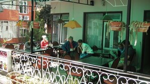 Un café al aire libre con mesas y sillas, rodeado por una valla de metal decorativa y plantas en macetas.