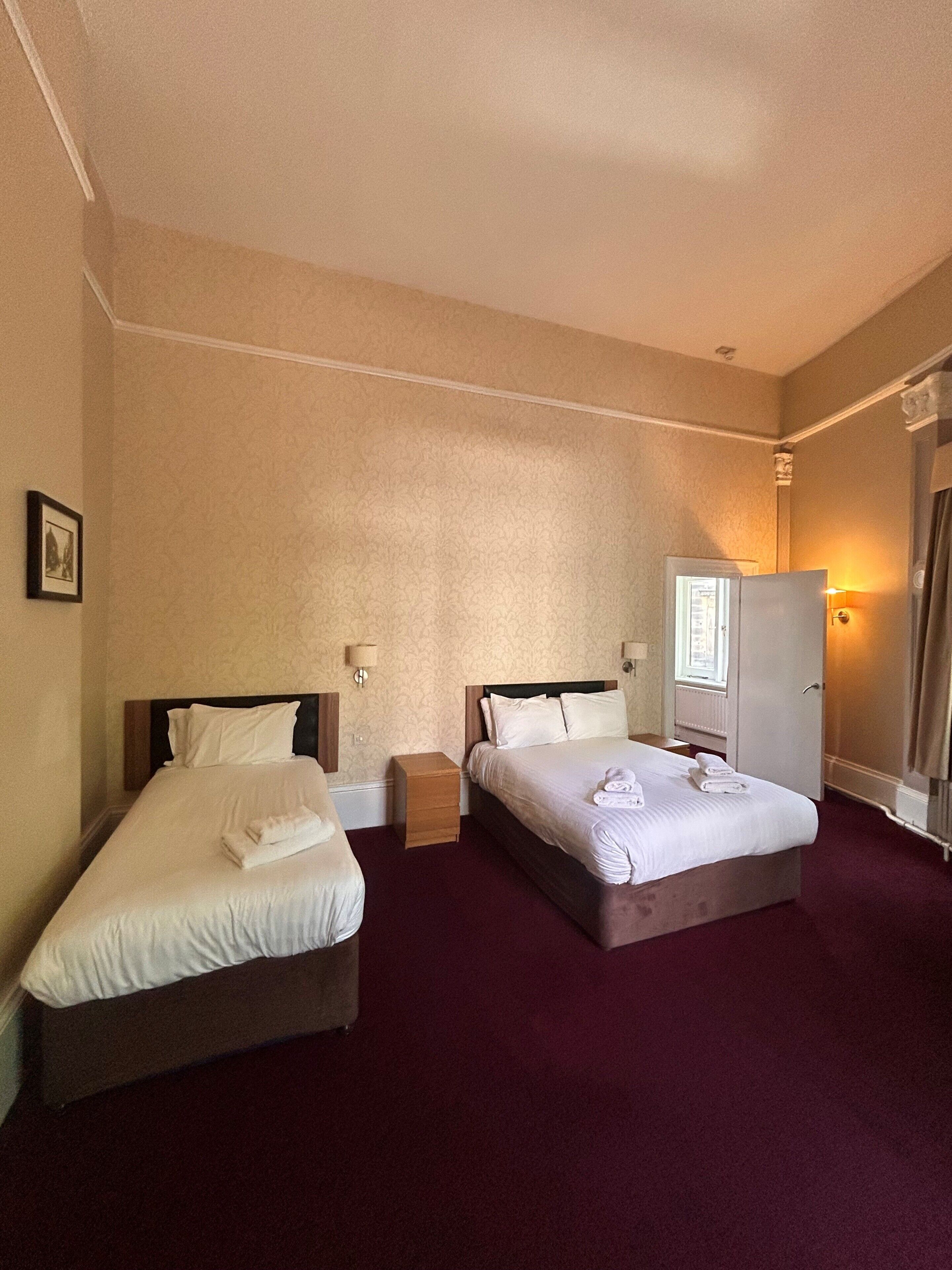 Quarto de hotel com duas camas, um guarda-roupa, uma mesa de cabeceira e um abajur.