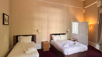 Quarto de hotel com duas camas, um guarda-roupa, uma mesa de cabeceira e um abajur.