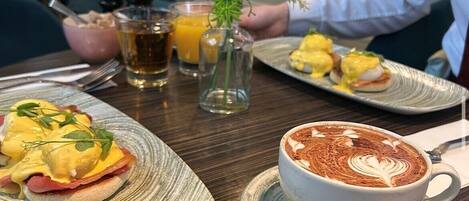 Una mesa de comedor con platos de comida, una taza de café y un pequeño jarrón con plantas.