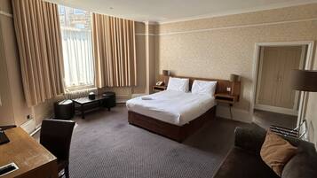 Una habitación de hotel con cama, escritorio, sofá y ventana con cortinas.