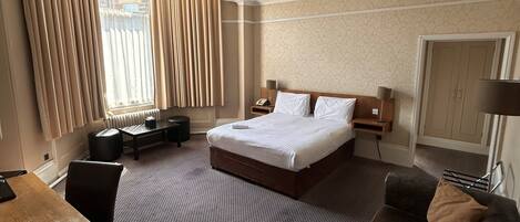 A hotel room with a bed, a desk, a sofa, and a window with curtains.