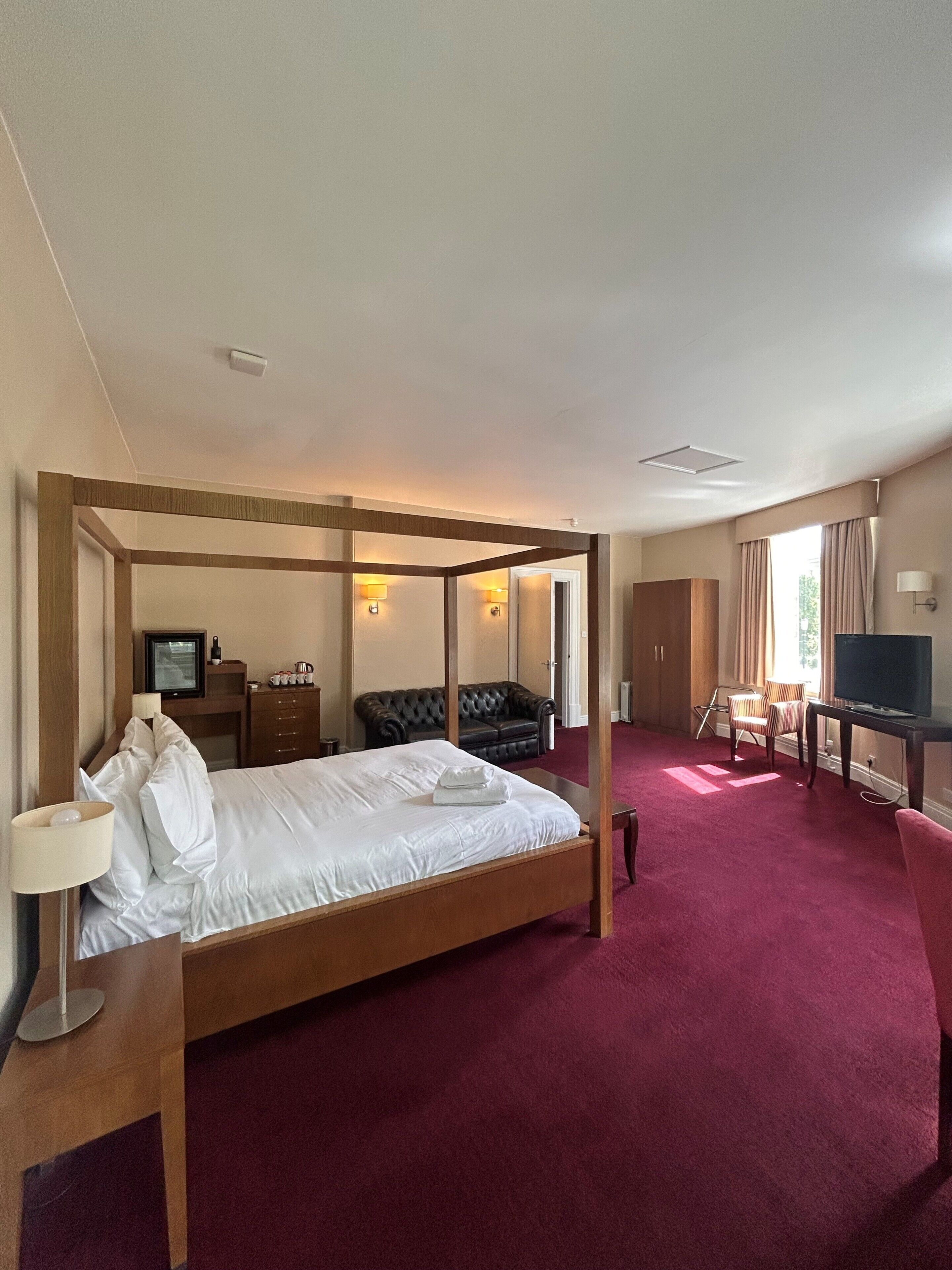 Habitación de hotel con cama con dosel, televisor, escritorio con silla y sofá.