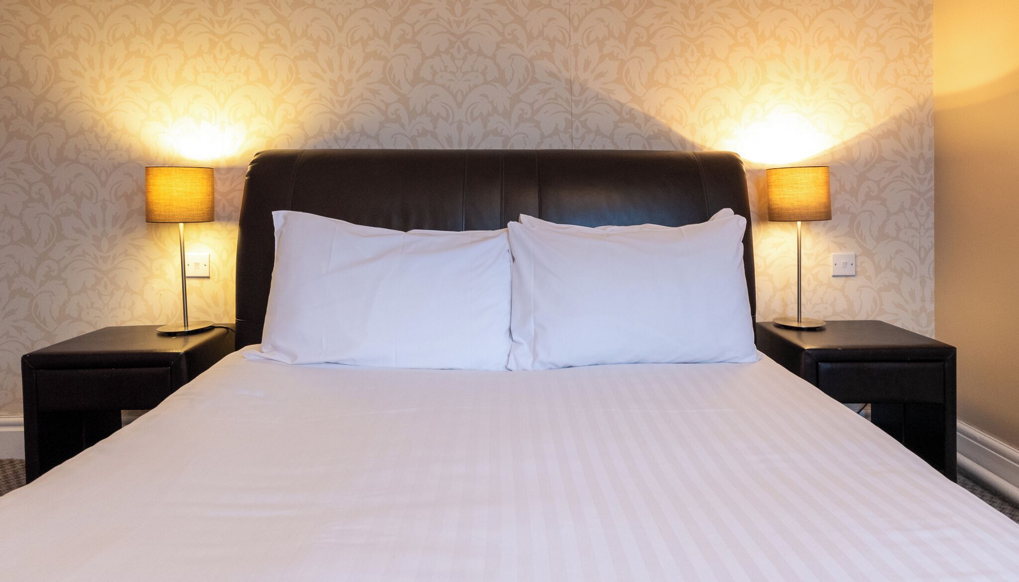 A hotel room with a large bed, two bedside lamps, and a patterned wallpaper.
