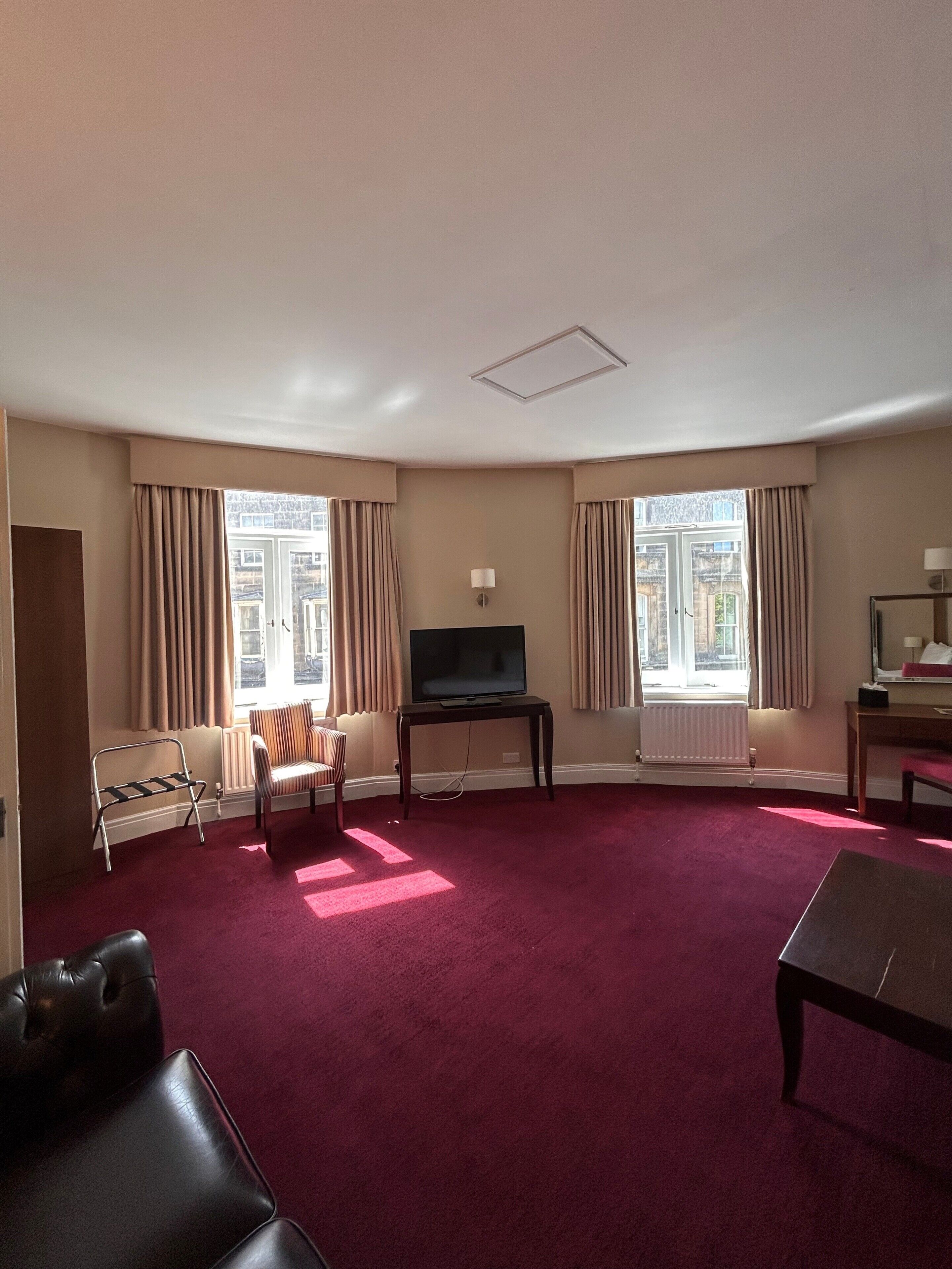 A hotel room with a flat-screen TV, a sofa, a chair, a small table, and a window with curtains.