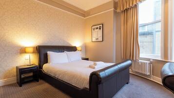 A hotel room with a large bed, two bedside lamps, a radiator, and a window with curtains.