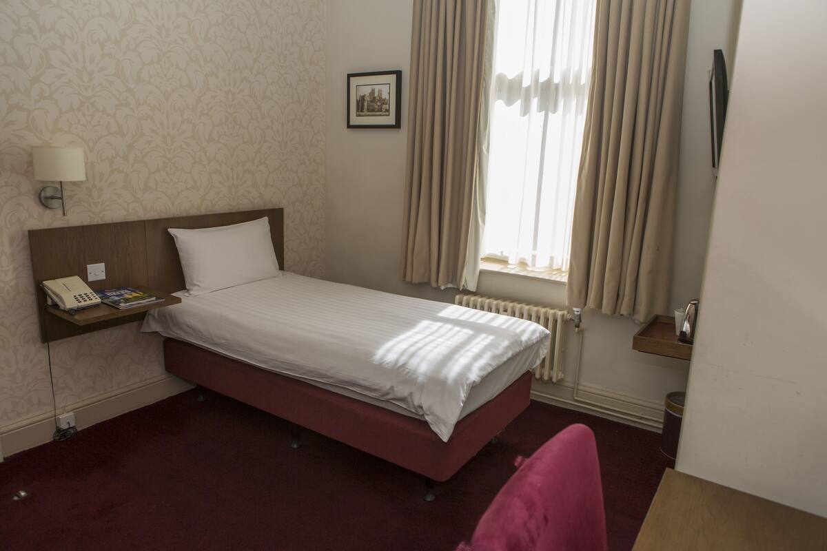 A hotel room with a bed, a bedside table with a lamp, a telephone, and a picture on the wall.