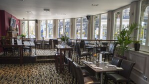 A restaurant with a patterned floor, multiple tables and chairs, and large windows offering a view of the street. - Crown Hotel Harrogate (Harrogate)