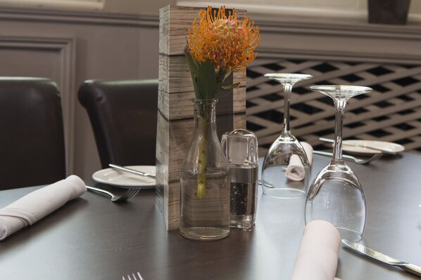 Une table à manger dressée avec un vase de fleurs, des salières et des poivrières, et des verres à vin.