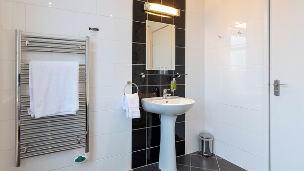 A modern bathroom with a white sink, a towel rack, a mirror, and a small trash bin. - Crown Hotel Harrogate (Harrogate)
