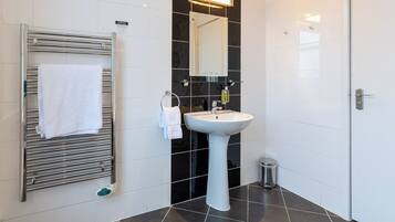 Un baño moderno con un lavamanos blanco, un perchero, un espejo y un cubo de basura pequeño.