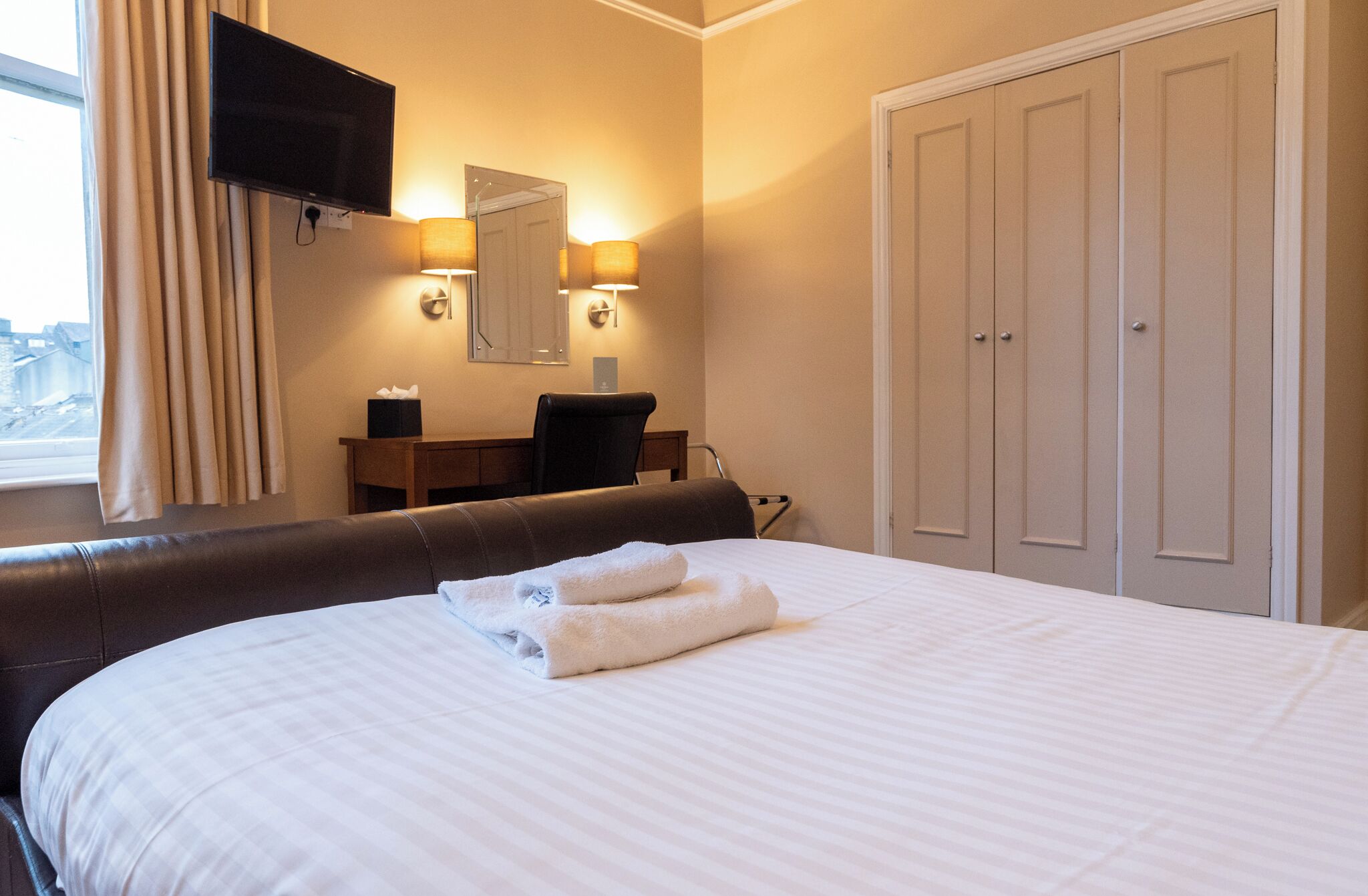 Una habitación de hotel con cama, escritorio, silla, televisor y armario.