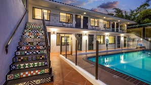 Une maison à deux étages avec une piscine, un escalier orné de carreaux colorés et un balcon.