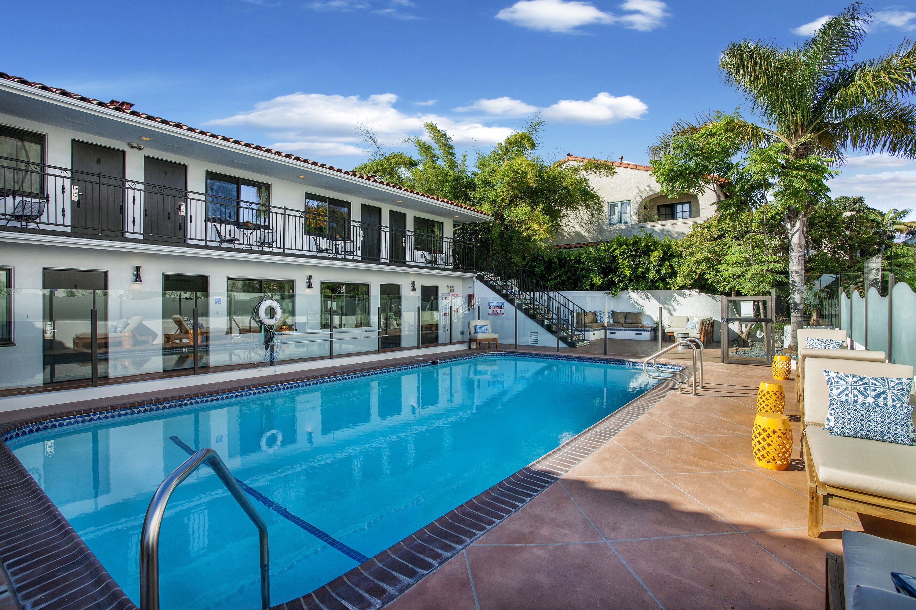 A hotel with a swimming pool, outdoor seating, and a staircase leading to the upper floors.