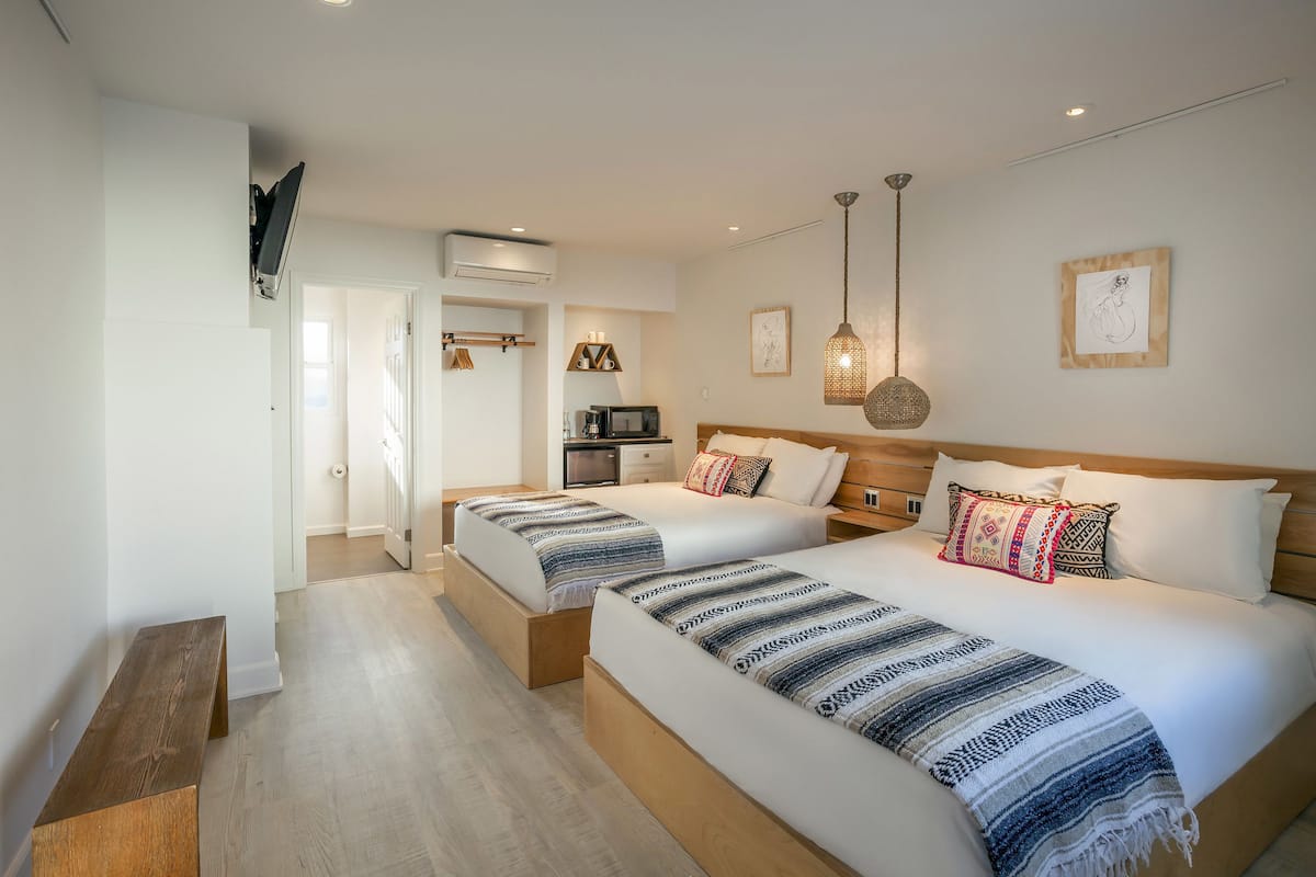 A hotel room with two beds, a TV, a microwave, and a wooden bench.