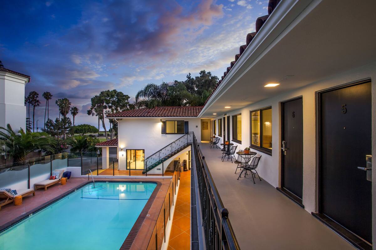 A hotel with a pool, outdoor seating, and a staircase leading to the upper level.