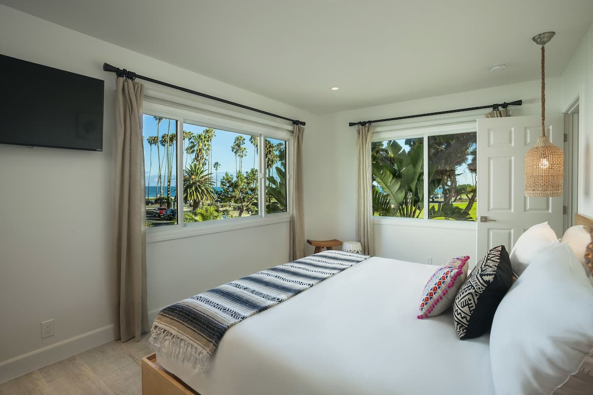 A bedroom with a bed, windows, a TV, and a door.
