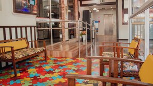 A lobby with wooden furniture, a colorful puzzle carpet, and a large window. - Pousada Caroline (Foz do Iguaçu)