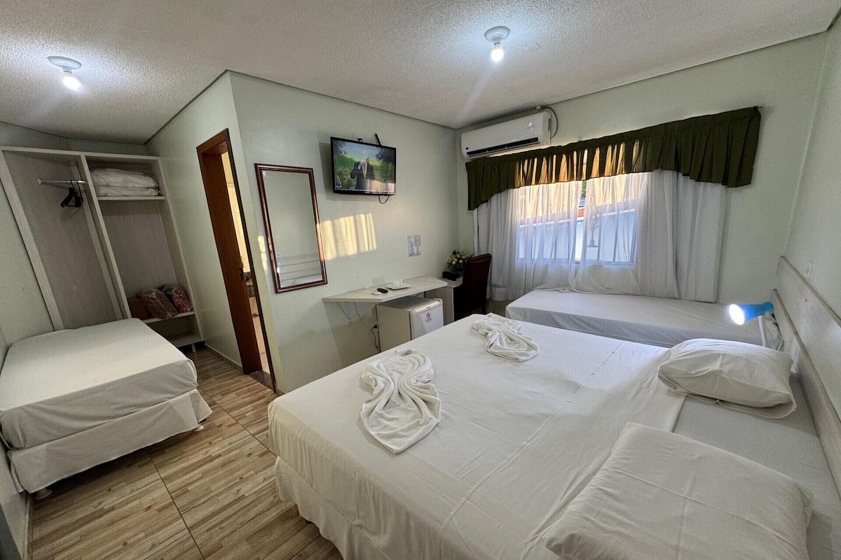 A hotel room with two beds, a desk, a mirror, an air conditioning unit, and a window with curtains.